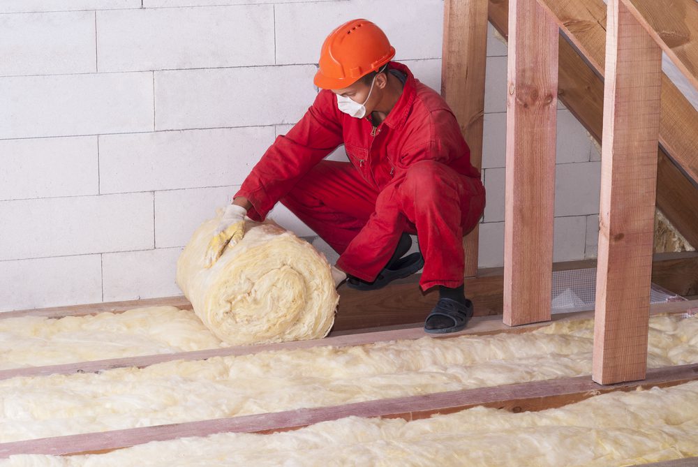 man in red uniform lays insulation in attic