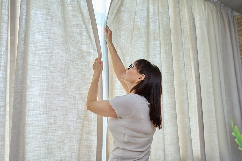 woman closing curtains at window