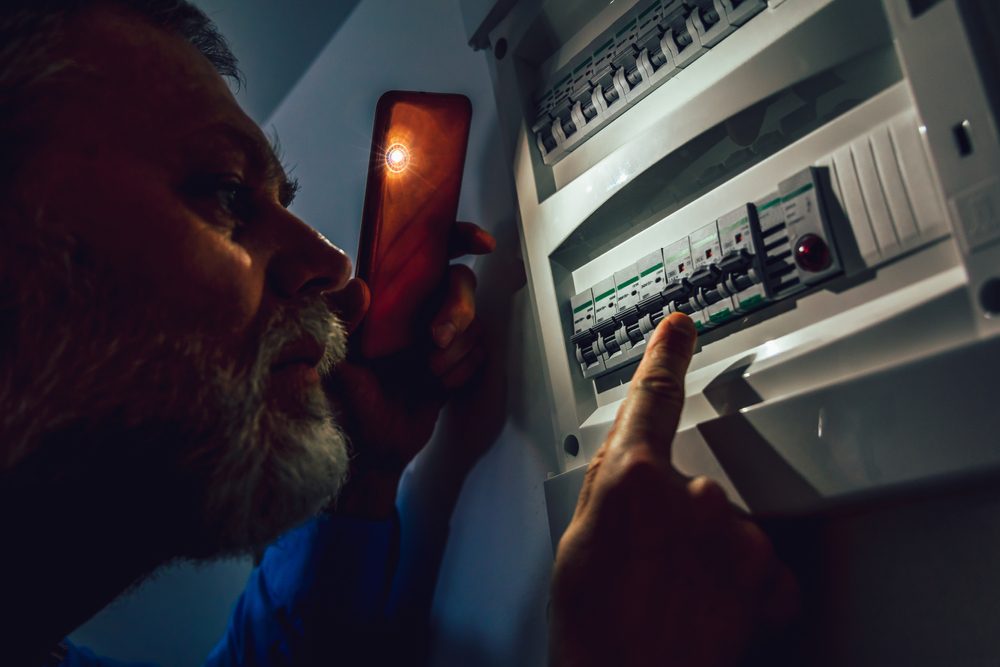 man checks electrical panel with phone light during power outage