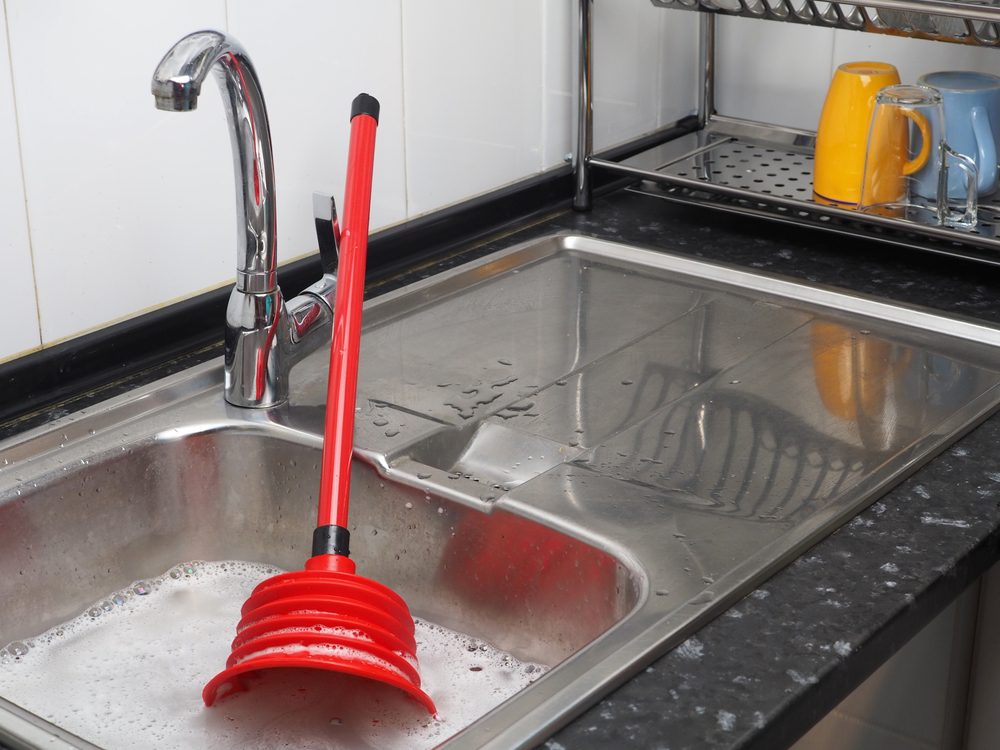 kitchen sink with soapy water and red plunger