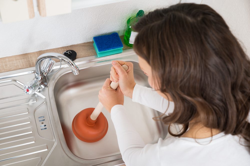 woman with plunger unclogging kitchen sink